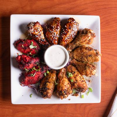 Variety of chicken wings arranged on a white platter with a dipping sauce.