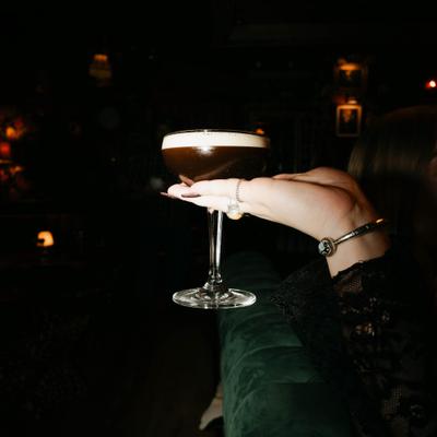 A hand with a bracelet holds an elegant, frothy cocktail in a coupe glass.