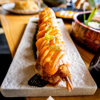 A salmon-topped sushi roll with sauces, green roe, and a shrimp tail..