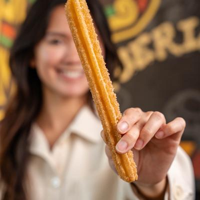 Person holding a freshly fried churro dusted with sugar.
