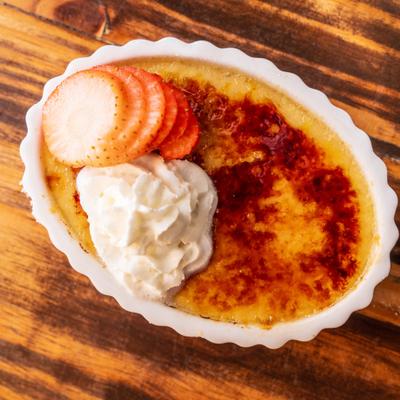 Torched caramel custard dessert topped with whipped cream and sliced fresh strawberries.