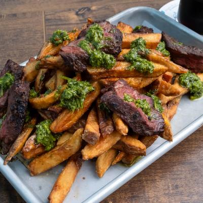 Grilled hanger steak slices served over a pile of crispy hand-cut fries.