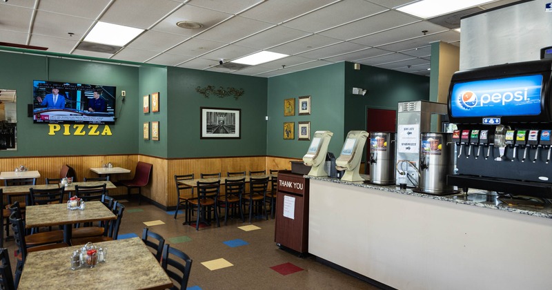 Interior of a pizzeria with tables and chairs, green walls, a wall mounted television