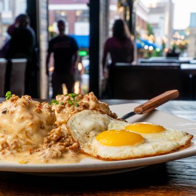 A plate of Biscuits and gravy with over easy eggs, sits on a wooden table.