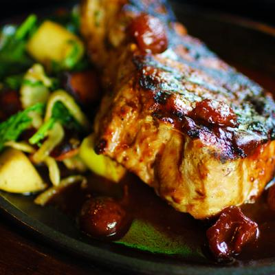 Pork chop with bacon, sauce, and roasted potatoes.