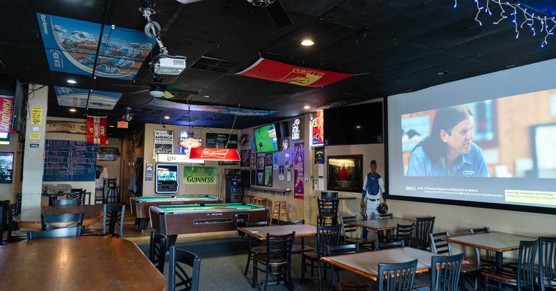 Interior of a bar with tables and chairs, a pool table, and a large projection screen