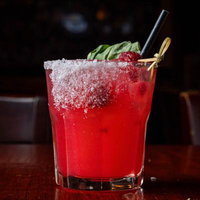 A fresh red mocktail, with sugared rim, berry and herb leaf garnish.