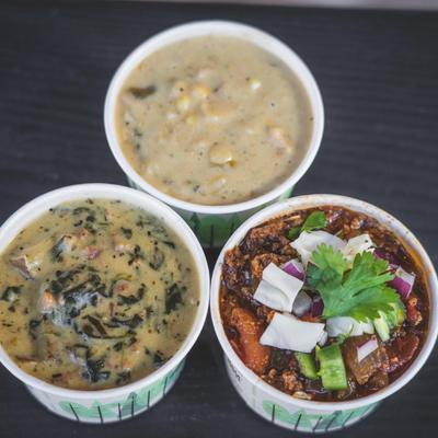 Three paper cups of chili and creamy soups on a dark table.