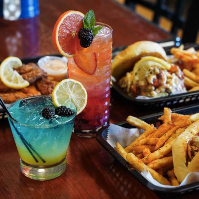 Two colorful cocktails and fried dishes on a table.