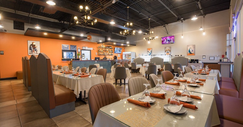 Interior - tables set with dishes and glasses, orange accent walls, cushioned seating & a bar area