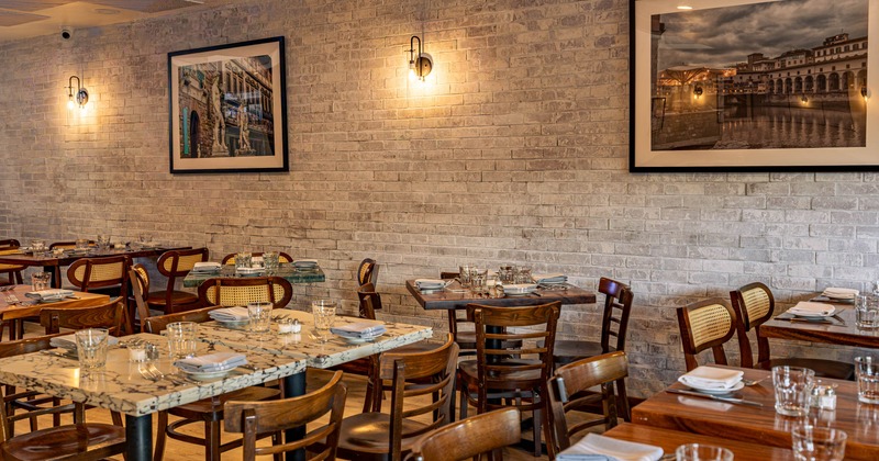 Inside, dining room with set wooden tables, woven back chairs, two framed city photographs