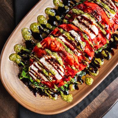 Caprese salad with arugula and drizzle of pesto and balsamico glaze.