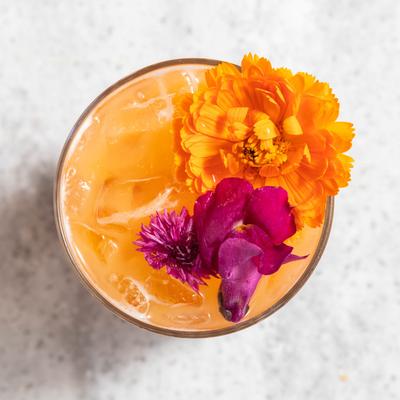 An overhead view of a cocktail topped with vibrant orange and purple flowers.