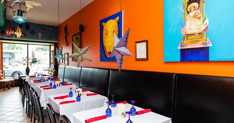 Banquette seating and set tables by an orange wall adorned with paintings
