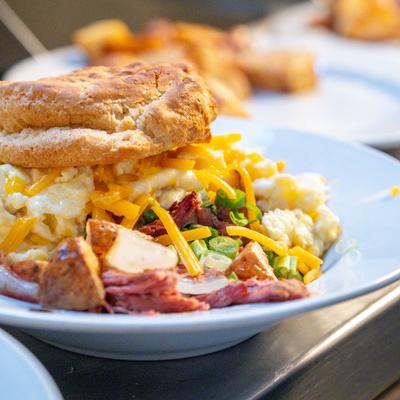 A biscuit sandwich with eggs, cheddar, and green onions, served with corned beef hash.