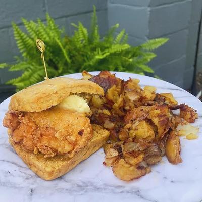 A crispy fried chicken sandwich with butter on a biscuit, served with smashed potatoes.