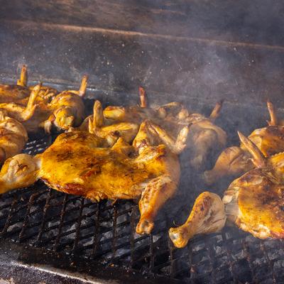 Multiple whole chickens grilling over hot coals on a barbecue grate.