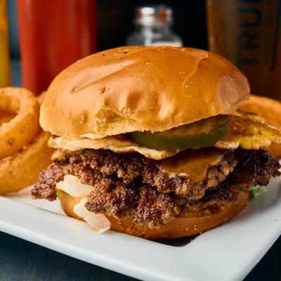 Smash burger topped with fried egg and pickles, served with onion rings.