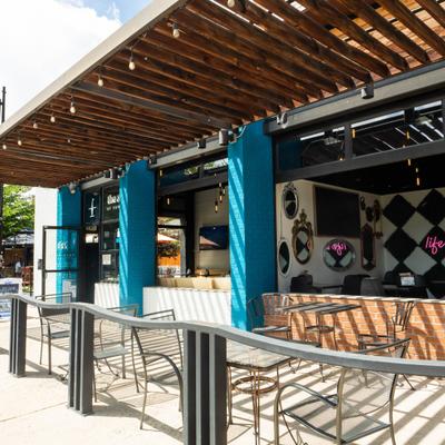 Fenced outdoor patio featuring table seating, a blue exterior wall and a neon sign.