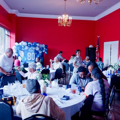 People gathered in a room for a 80th birthday celebration.