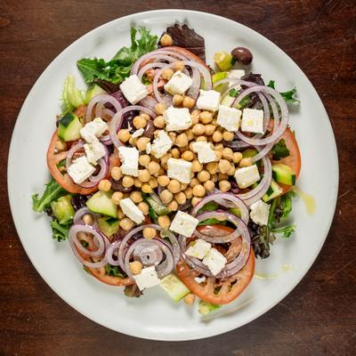 Top-down view of a chickpeas salad topped with feta cheese, tomatoes, cucumbers, and olives.