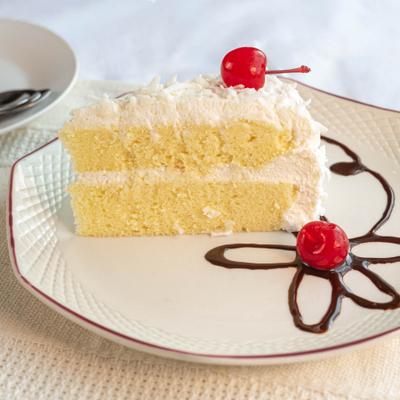 A slice of coconut cake garnished with cherries, served on a plate with chocolate drizzle.