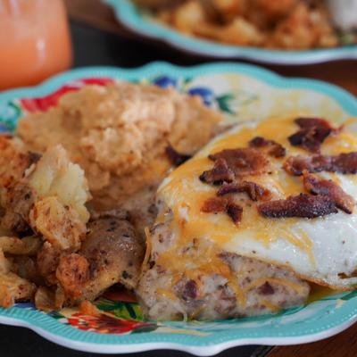 Cheesy fried egg topped with bacon, served with smashed potatoes and grts.