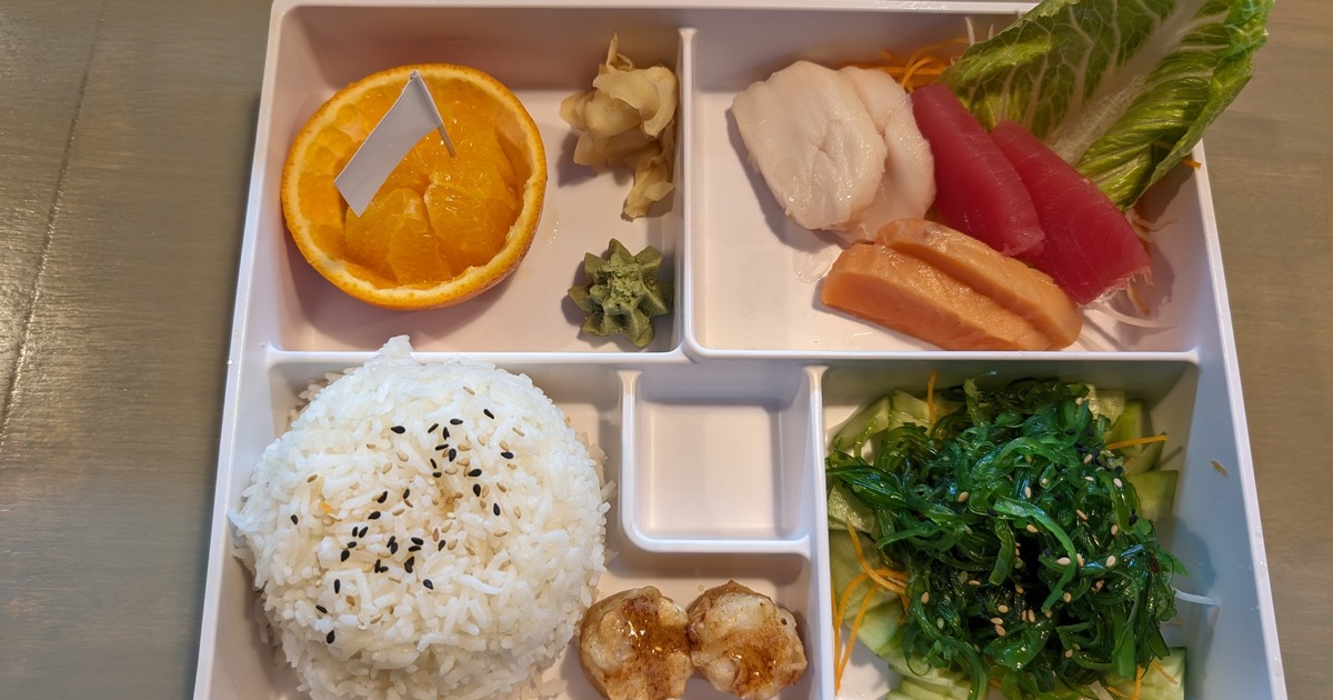 Japanese-style bento box featuring rice, sashimi, and various sides