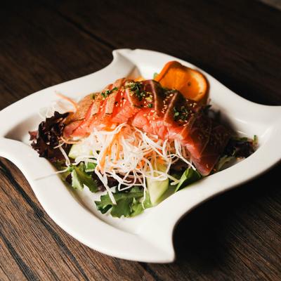 A plate of salmon sashimi served over shredded daikon radish and vegetables.