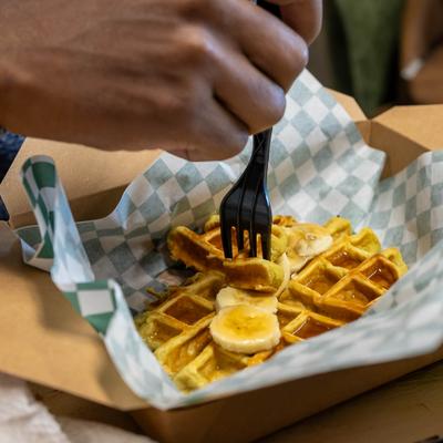Hand taking a bite of banana-topped waffle with a fork.