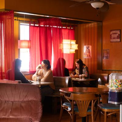 Interior with people seating at the booths next to a window with red curtains.