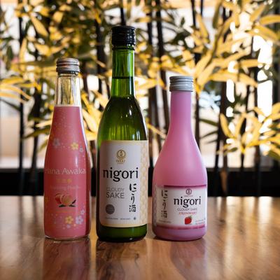 Three bottles of flavored sake on a table with a leafy background.