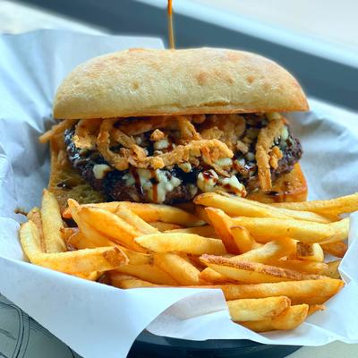 Burger topped with crispy onions and sauce served with golden fries on a white paper.