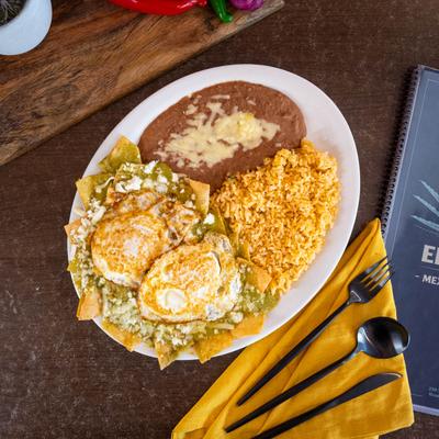Chilaquiles verdes topped with fried eggs, served with beans and rice.
