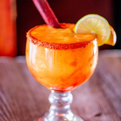 Mangonada cocktail in goblet with chili rim, lime, and Mexican candy stick.