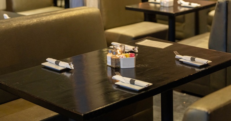 Interior - dark wood tables with napkins and cutlery, surrounded by leather booth seating