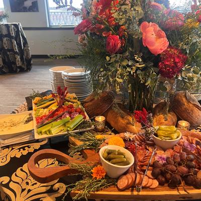 Buffet table with floral arrangement, charcuterie board, loaves of bread, and plates.