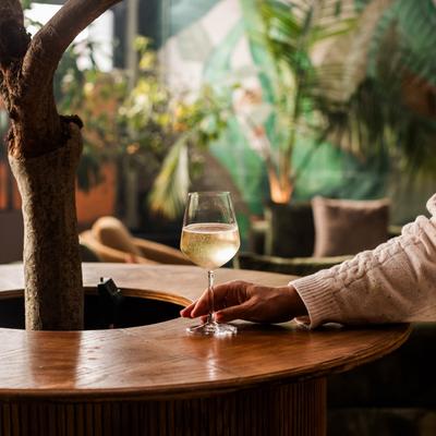 A person enjoys a glass of white wine at a decorative coffee table.