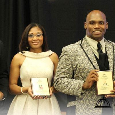 Two people displaying award plaques.