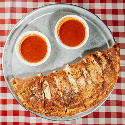A tray of calzone with two cups of red sauces, sits on a  a red and white checkered tablecloth.