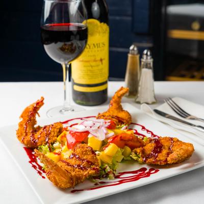 Coconut shrimp served with fresh vegetables, alongside glass of red wine.