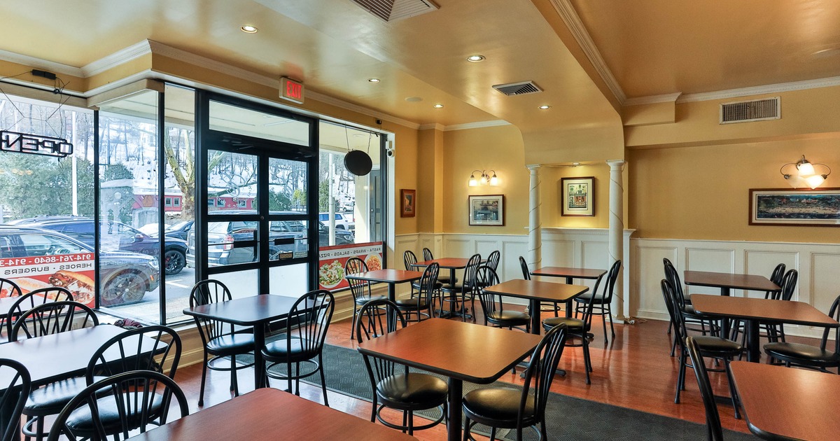A small warmly lit restaurant with wooden tables, black chairs and large windows.