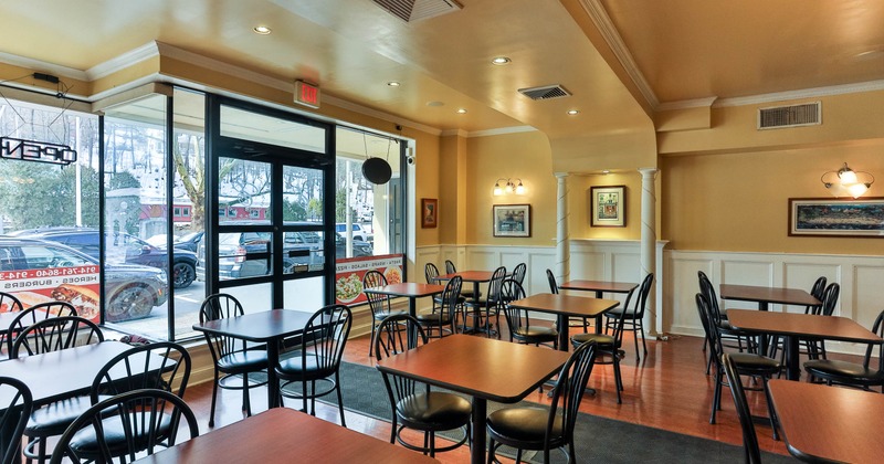 A small warmly lit restaurant with wooden tables, black chairs and large windows.