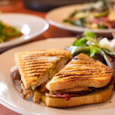 Chicken Pesto Melt plate with food plates in the background, close up.