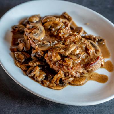 Steak covered in a rich mushroom and onion gravy on an oval white plate.