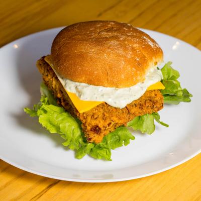 Fried chicken sandwich with lettuce, cheese, and sauce on a plate.