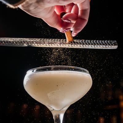 Cinnamon stick being grated over the cocktail in coupe glass.