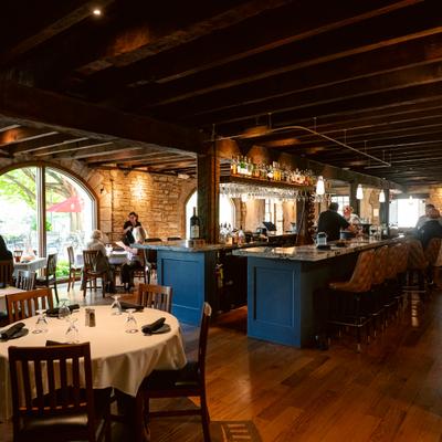 Interior with exposed wooden beams, limestone brick walls, table seating and a bar area.