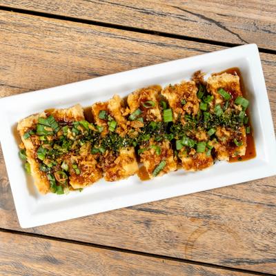 Fried tofu topped with sauce, herbs and chopped green onions.