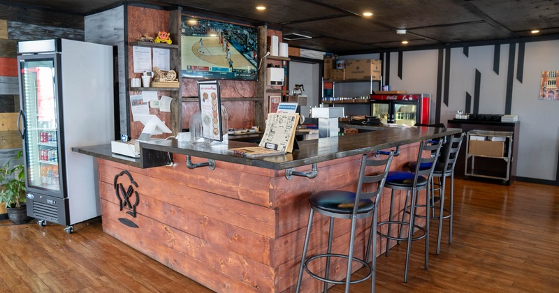 A cozy bar with a wooden counter, metal stools, and a TV
